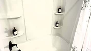A white bathtub with a shower curtain, a faucet, and two shelves with bottles.