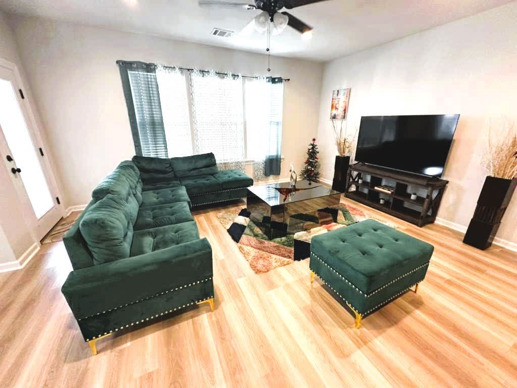 A living room with a sectional sofa, ottoman, and a flat-screen TV.