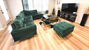 A living room with a sectional sofa, ottoman, coffee table, and a flat-screen TV. - Game Day Touchdown Lounge in Baton Rouge  - CB1024 (Baton Rouge)