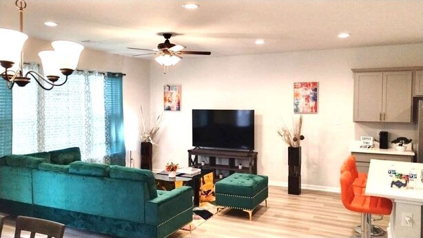 A living room with a sofa, ottoman, TV, and a small table with decorative items. - Game Day Touchdown Lounge in Baton Rouge  - CB1024 (Baton Rouge)