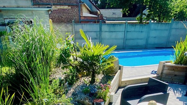 A poolside area with a curved patio, outdoor seating, and a variety of plants and flowers. - Les 3 E (Englebelmer)