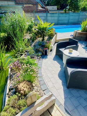 A poolside area with a curved patio, outdoor seating, and a variety of plants and flowers. - Les 3 E (Englebelmer)