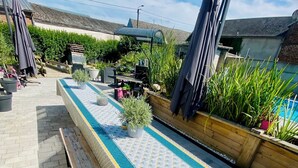 A pool table with a patterned tablecloth, surrounded by potted plants and outdoor furniture. - Les 3 E (Englebelmer)