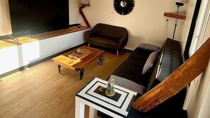 A modern living room with a large flat-screen TV, a brown sofa, a coffee table, and a unique wall clock. - Les 3 E (Englebelmer)