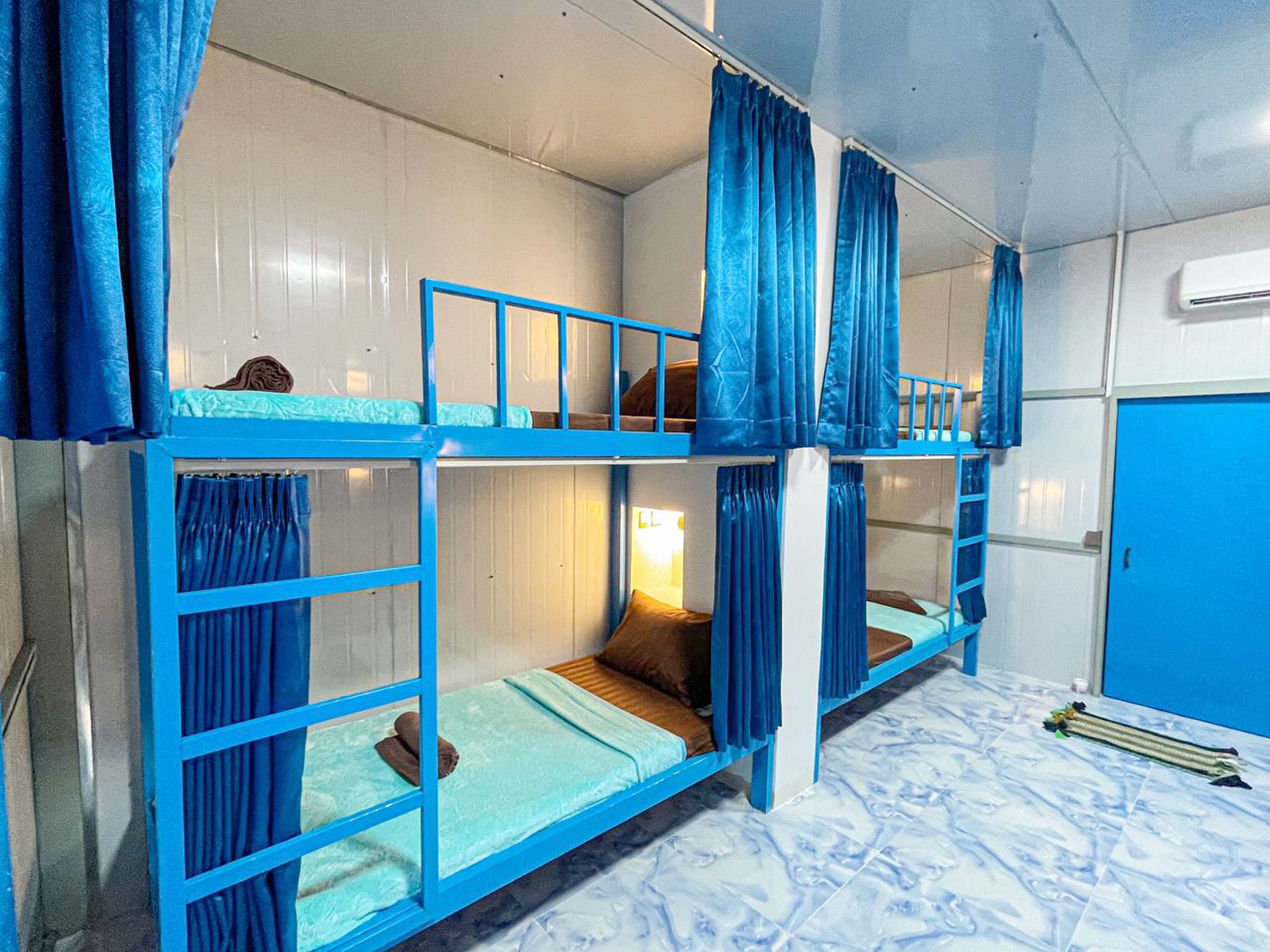 Camera con letto a castello, tende blu, un tavolino con lampada e una porta blu.