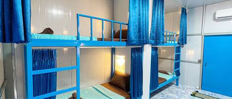 Camera con letto a castello, tende blu, un tavolino con lampada e una porta blu.