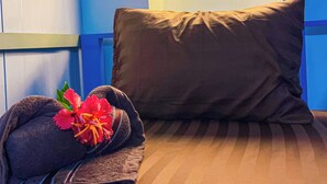 A neatly made bed with a brown pillow and a folded towel with a red flower on a striped carpet. - Blue Shore Pavilion (Koh Rong)