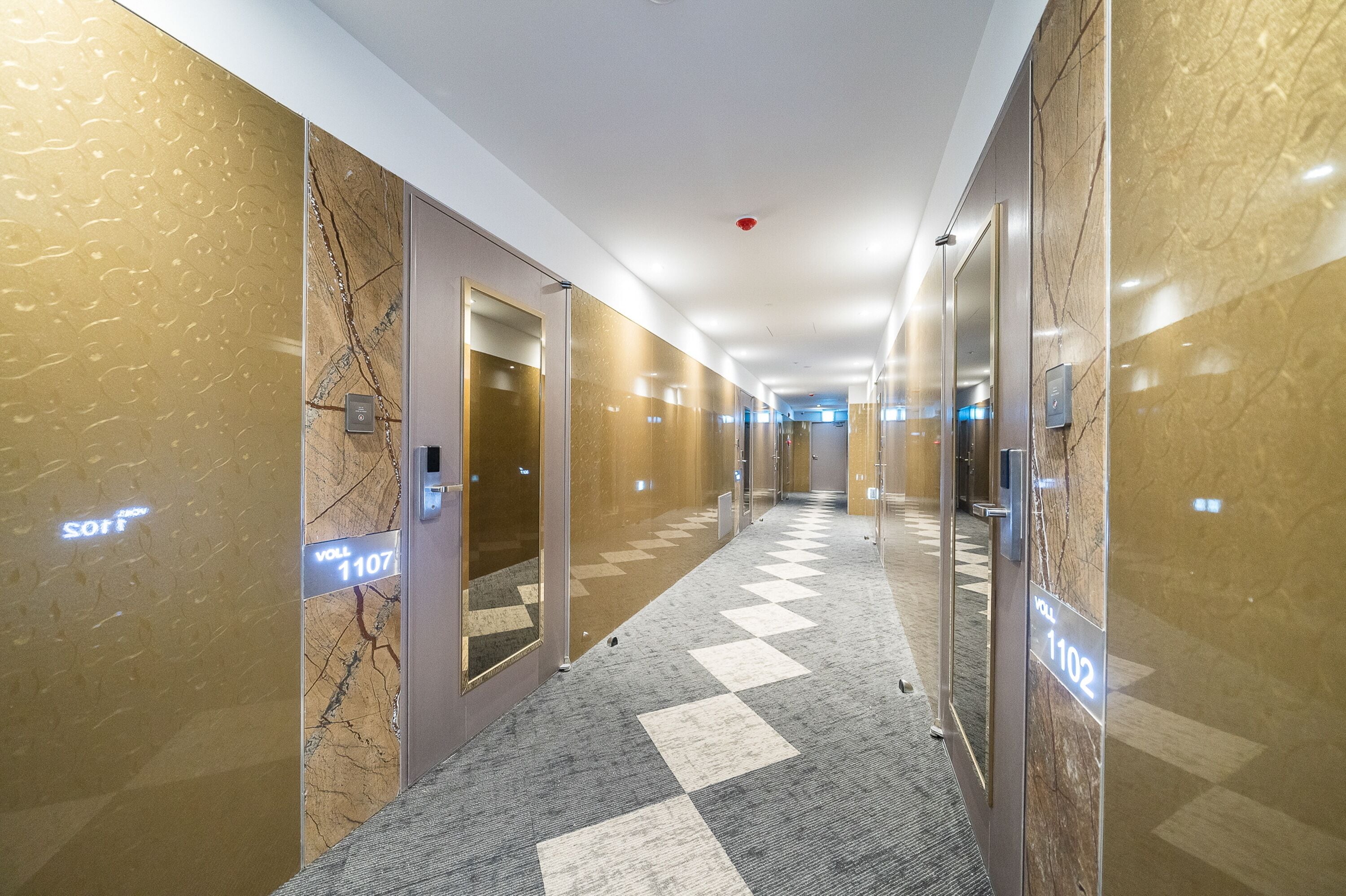 A hotel corridor with marble walls, checkered carpet, and numbered doors.