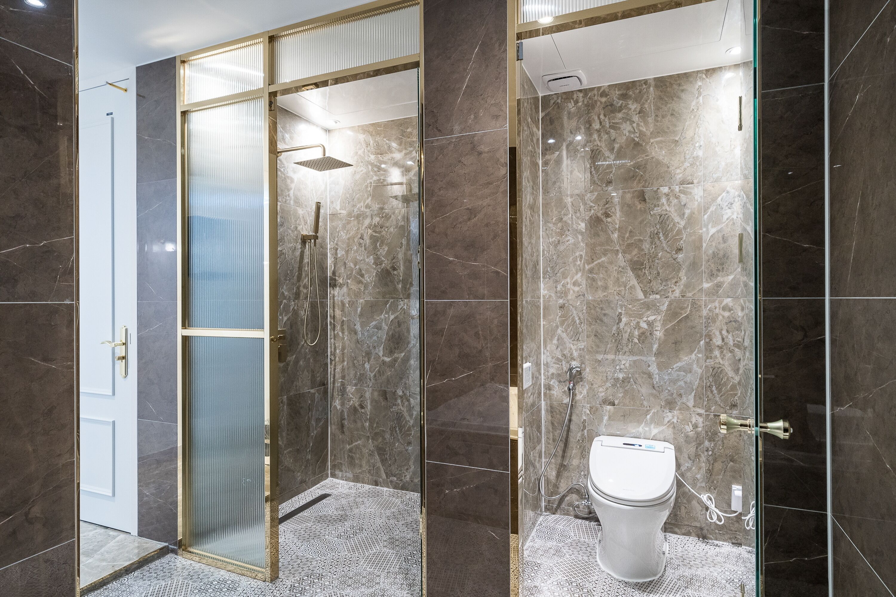 A modern bathroom with a glass-enclosed shower, a toilet, and marble flooring.