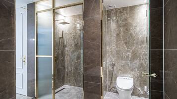 A modern bathroom with a glass-enclosed shower, a toilet, and marble flooring.
