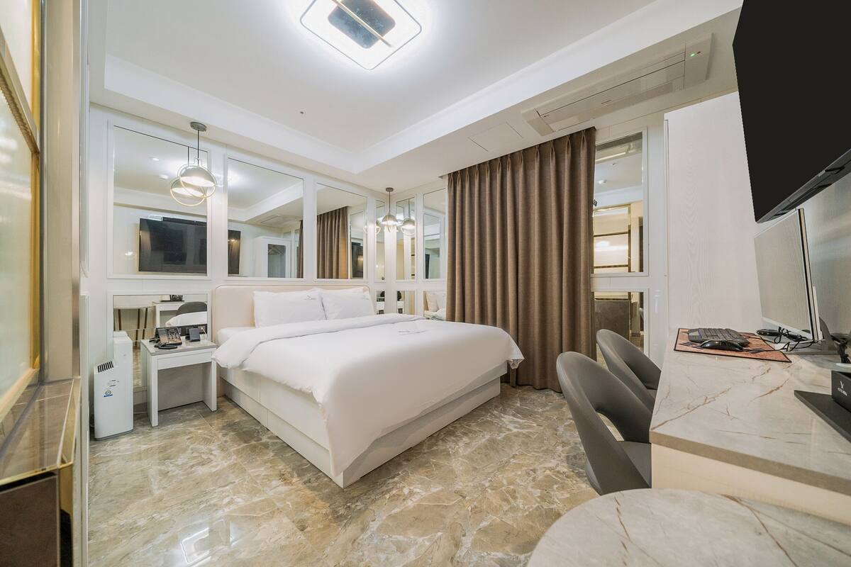 Une chambre d’hôtel moderne dotée d’un grand lit, d’un bureau avec un ordinateur, d’une télévision à écran plat et d’un grand miroir.