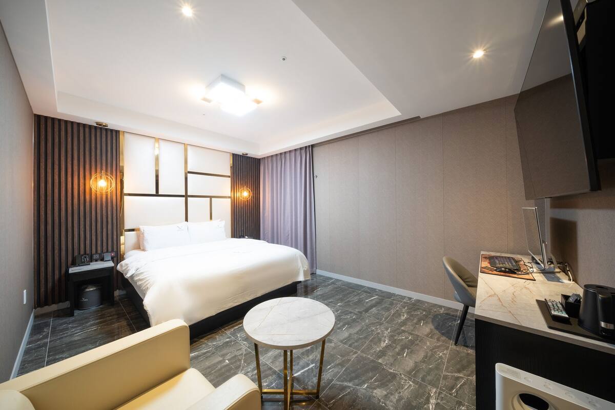 Une chambre d’hôtel moderne, dotée d’un grand lit, d’un bureau avec un ordinateur, d’une chaise et d’une petite table ronde.