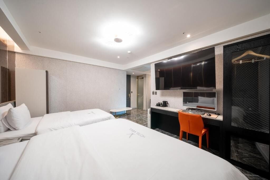 A hotel room with two beds, a desk with a computer, and a chair.