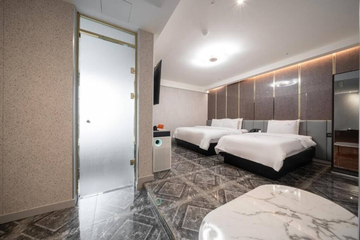 Une chambre d’hôtel moderne avec deux lits, un sol carrelé en marbre, un téléviseur à écran plat et un grand miroir.