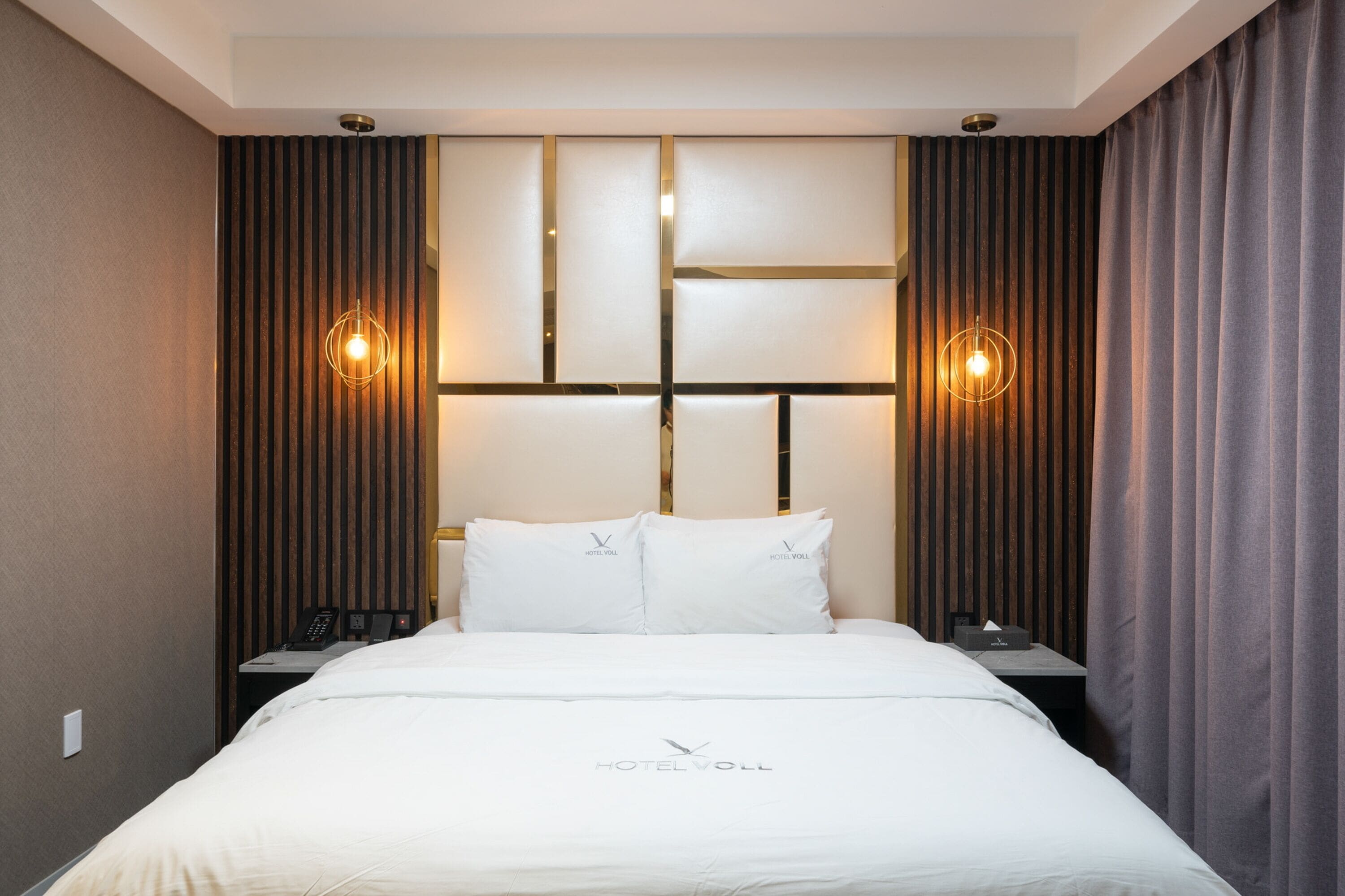 Ein Hotelzimmer mit einem großen Bett, zwei Nachttischen, einem an der Wand befestigten Fernseher und einem Kopfteil mit vertikalen Holzleisten.