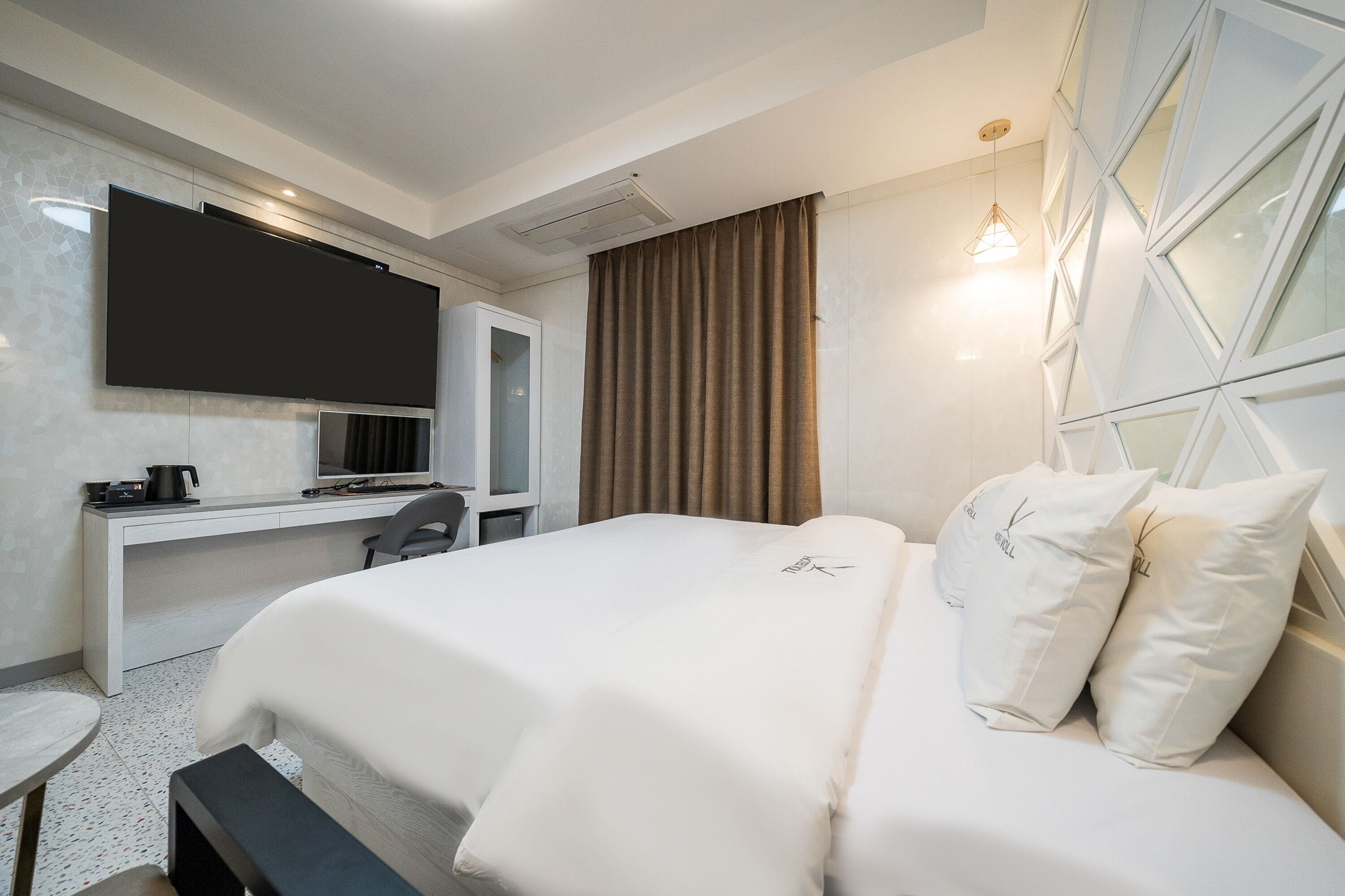 Quarto de hotel moderno com uma cama grande, uma escrivaninha com televisão de tela plana, uma cafeteira e uma janela ampla com cortinas.