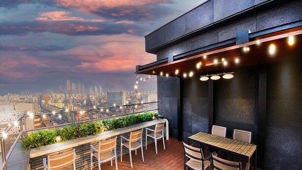 A rooftop bar with a city view, featuring a bar counter, seating area, and string lights.