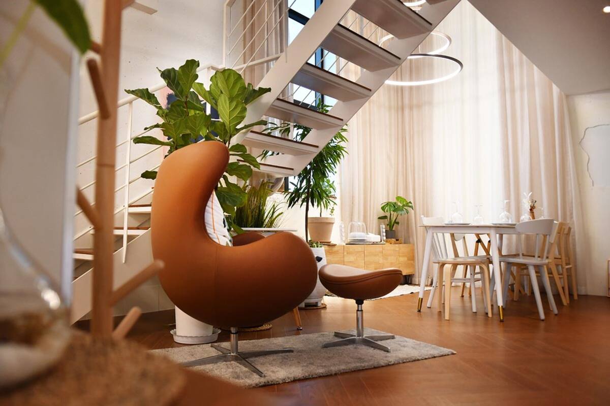 Un salon moderne avec un canapé aux lignes courbes, une table à manger avec des chaises et un escalier agrémenté d’une plante sur la plateforme.