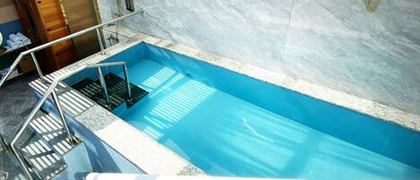 A swimming pool with a glass enclosure, a wooden cabinet, and a towel rack.