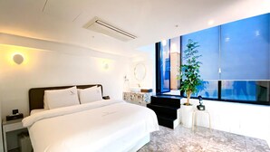 A modern hotel room with a large bed, a marble bathroom, a large window with a view, and a potted plant.