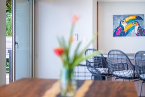 A dining area with a wooden table and chairs, a vase with flowers, and a colorful painting on the wall.