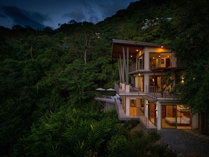 A multi-story modern house with glass doors and balconies, surrounded by dense forest. - Villa Vista del Mar by Pura Villas (Dominical)