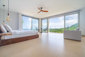 A modern bedroom with a large bed, a ceiling fan, and a balcony with a view of the landscape.