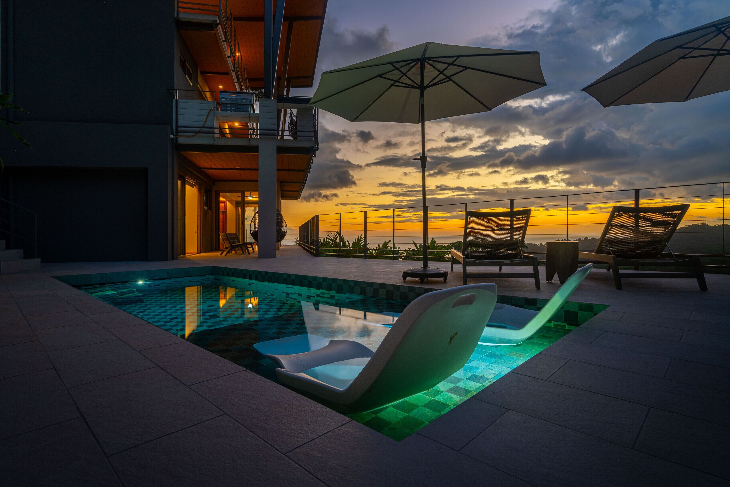 Un espace piscine aménagé sur le toit, avec des chaises longues et des parasols, offrant une vue sur le coucher du soleil.