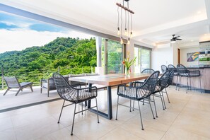 Un espace repas moderne avec une table en bois et des chaises en fil de fer noir, donnant sur une colline verdoyante.