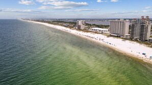 An aerial view of a beachside resort with multiple high-rise buildings, a sandy beach, and a clear view of the ocean.