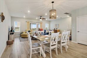A spacious dining area with a wooden table and white chairs, a ceiling fan, and a hanging light fixture.