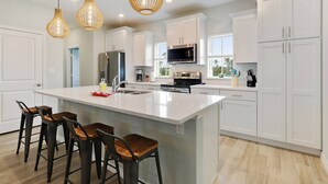 A modern kitchen with white cabinetry, a large island with bar stools, stainless steel appliances, and pendant lighting.