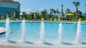 A pool with multiple water jets, green lounge chairs, and palm trees.