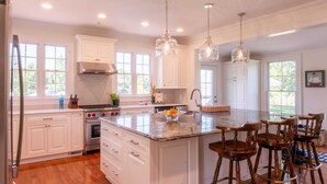 A spacious kitchen with white cabinets, a large island with bar stools, and pendant lighting. - Saint Michaels Summer Retreat with Pool & Hot Tub (Saint Michaels)
