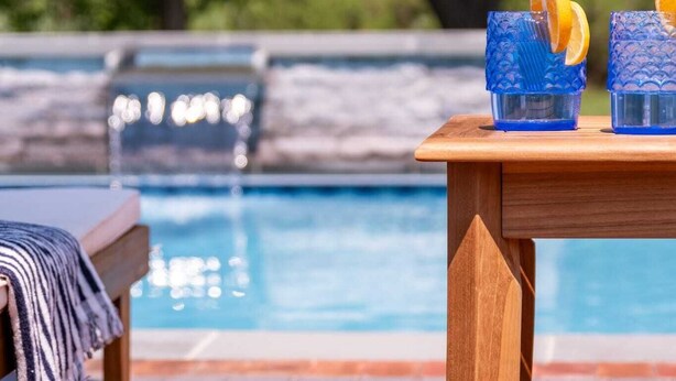A poolside area with a wooden table, a lounge chair, and a pool. - Saint Michaels Summer Retreat with Pool & Hot Tub (Saint Michaels)