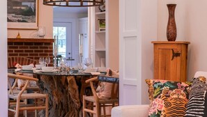 A dining area with a wooden table and chairs, a chandelier, and a sofa with colorful cushions. - Saint Michaels Summer Retreat with Pool & Hot Tub (Saint Michaels)