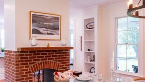 A dining area with a brick fireplace, a glass-top table, and wicker chairs. - Saint Michaels Summer Retreat with Pool & Hot Tub (Saint Michaels)
