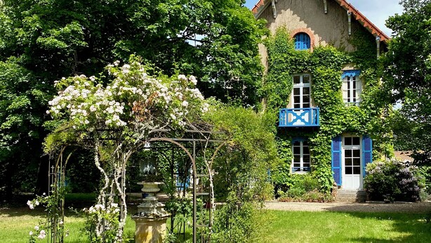 Une maison traditionnelle avec un jardin, comprenant une pergola couverte de plantes grimpantes et une fontaine.