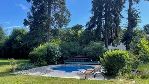 Un jardin à l’arrière de la maison, avec une piscine, entouré d’arbres et d’une pelouse verdoyante.