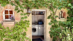 Une petite buanderie comprenant un lave-linge, un étendoir et une petite étagère sur laquelle sont rangés divers objets.