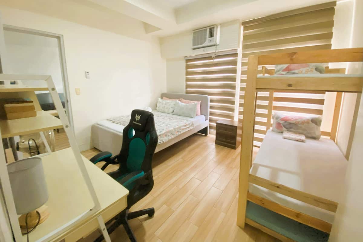 Un dormitorio con literas, un escritorio con silla, una cama con ventana y un radiador.