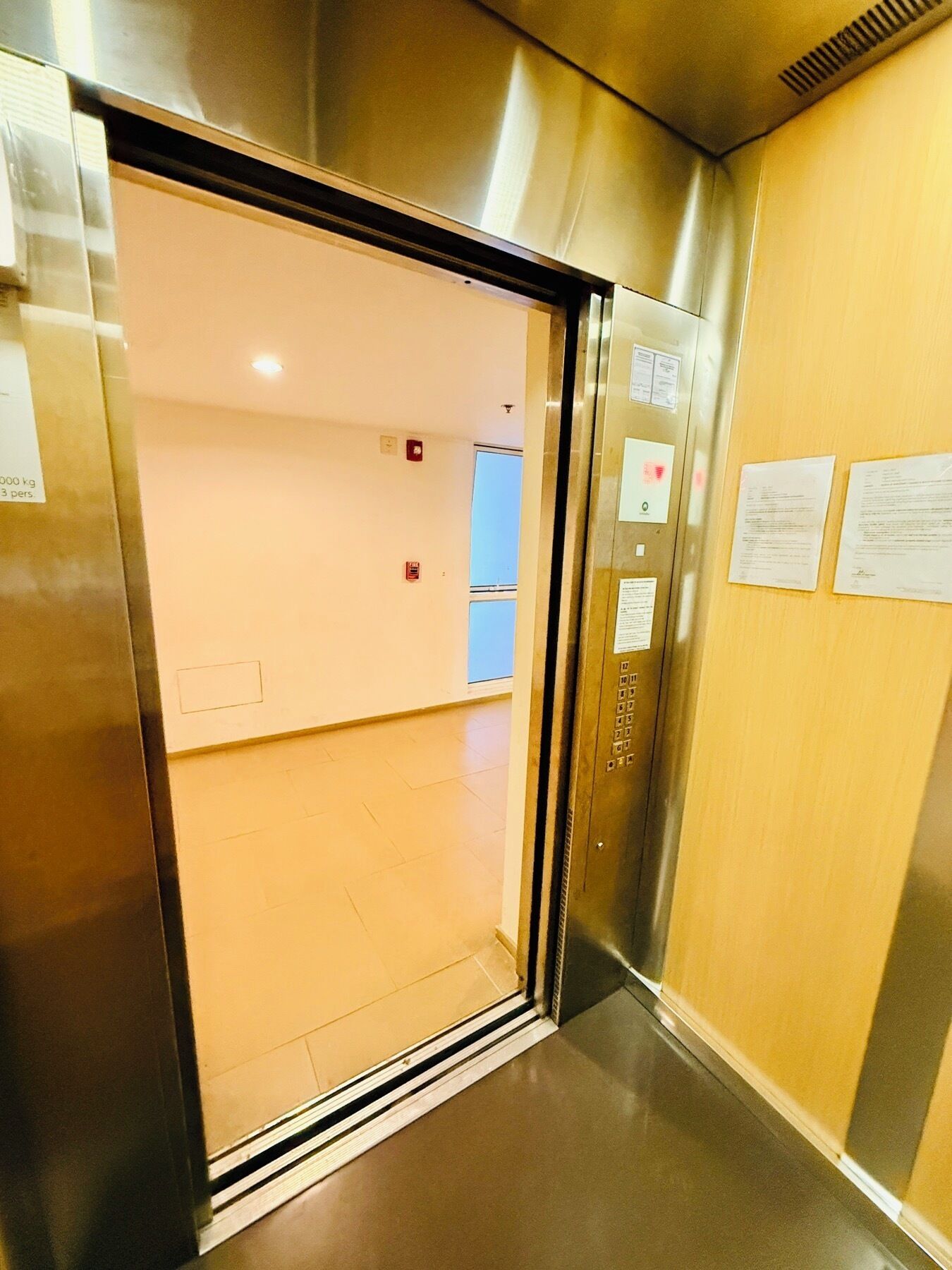 An elevator interior with metallic walls, a control panel, and emergency exit signs.