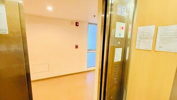 An elevator interior with metallic walls, a control panel, and emergency exit signs.
