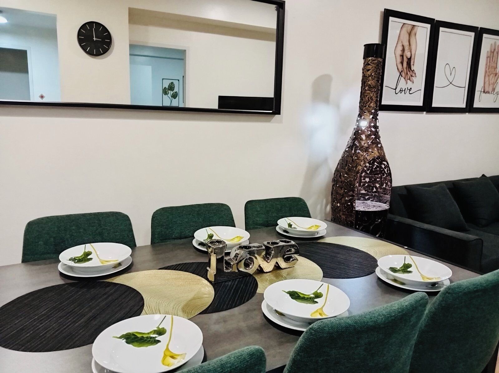 Un coin repas avec une table ronde, des chaises vertes et un vase décoratif.