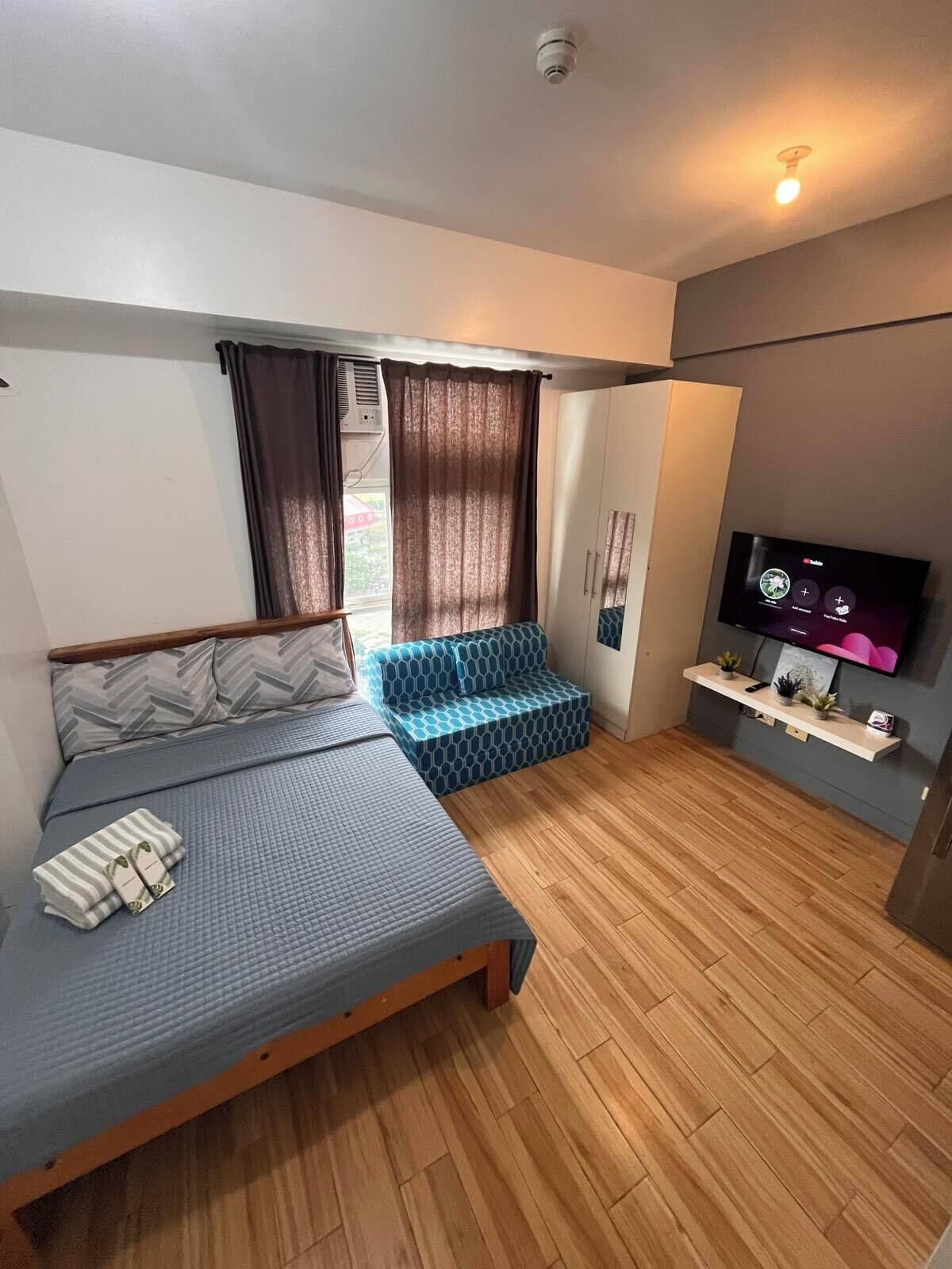 Een slaapkamer met een bed, een bank, een televisie en een klein plankje.
