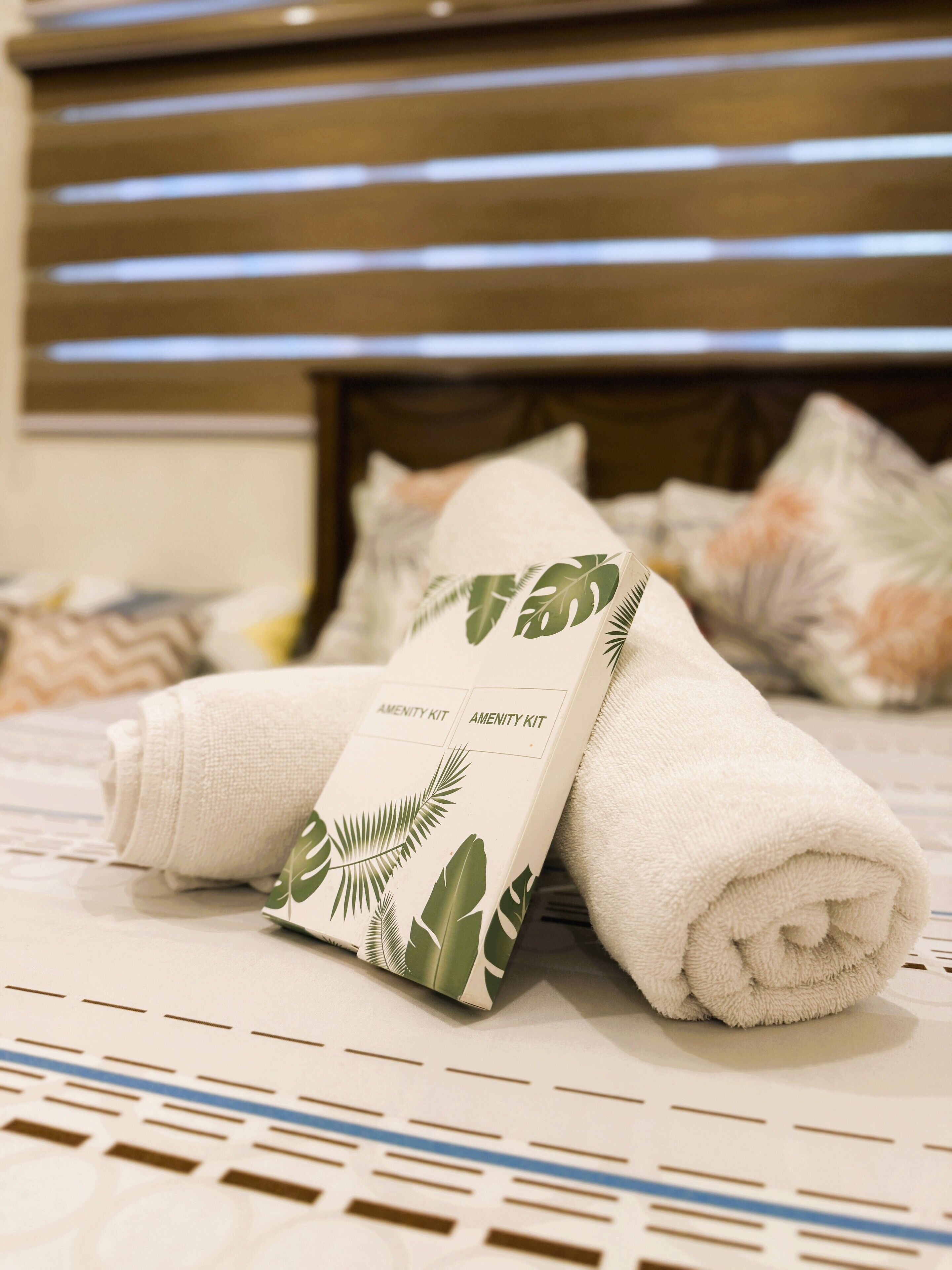 A neatly made bed with a white towel and a rolled-up towel on a patterned bedspread.