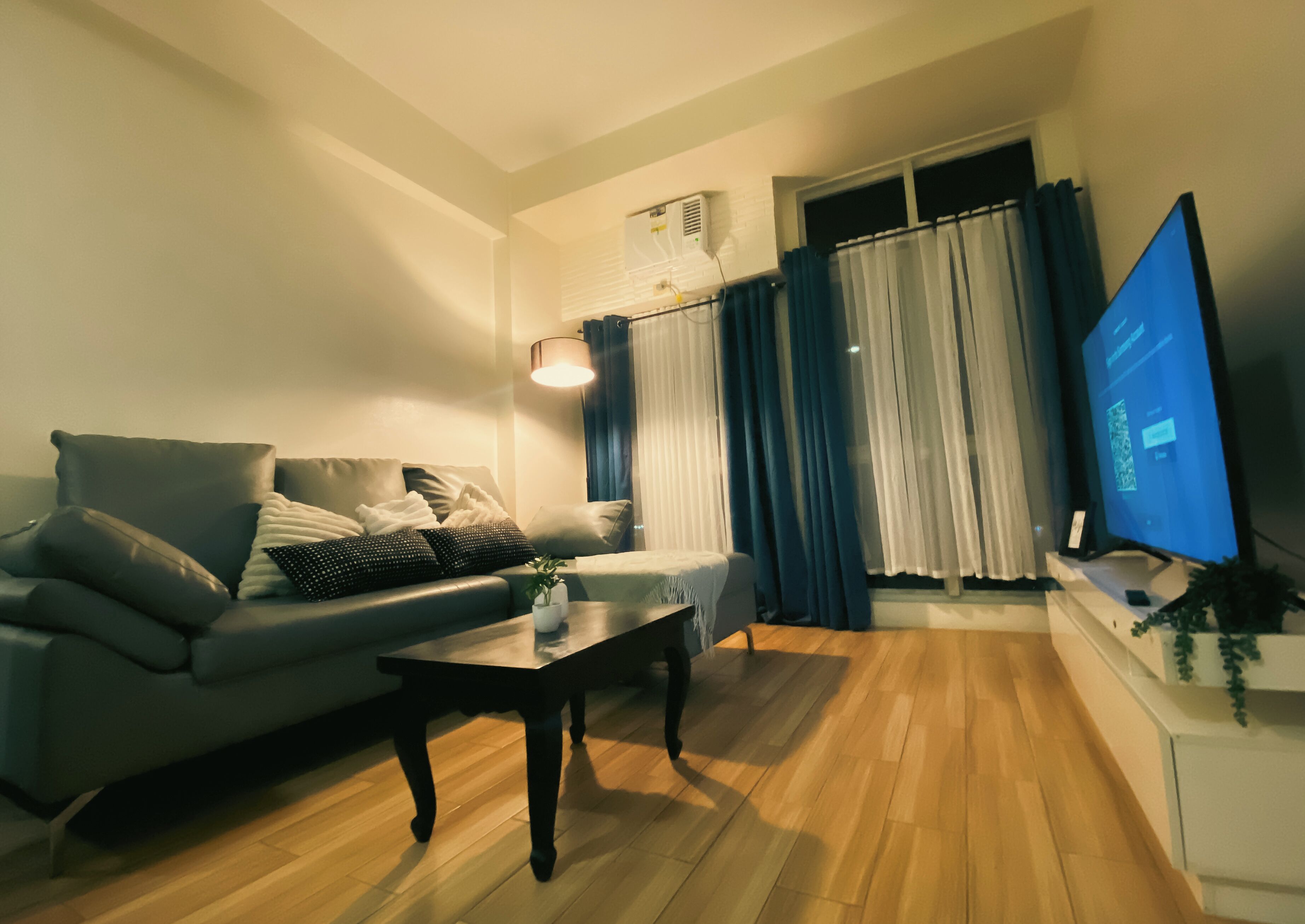 A living room with a sofa, a coffee table, a flat-screen TV, and a window with curtains.