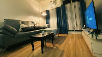A living room with a sofa, a coffee table, a flat-screen TV, and a window with curtains.