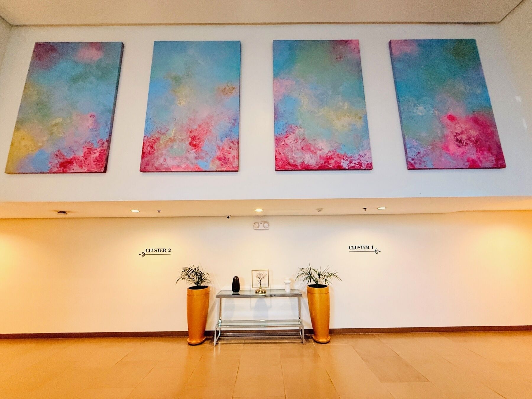 A reception area with a glass desk, two potted plants, and three abstract paintings on the wall.