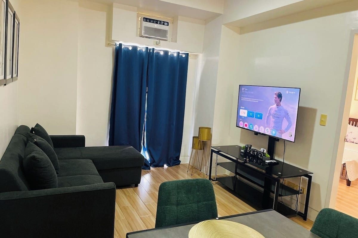 Una sala de estar moderna con un televisor de pantalla plana, un sofá, una mesa de centro y una mesita auxiliar.